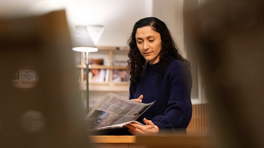 A dark-haired woman reading a newspaper.